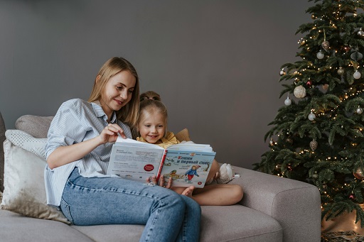 Mum near Christmas tree reading a book to little girl