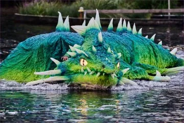 A vibrant green dragon-shaped boat with glowing eyes moves through the water, steered by a person dressed in matching attire.